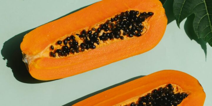 Top view of appetizing composition of ripe papaya with plant leaves on blue background
