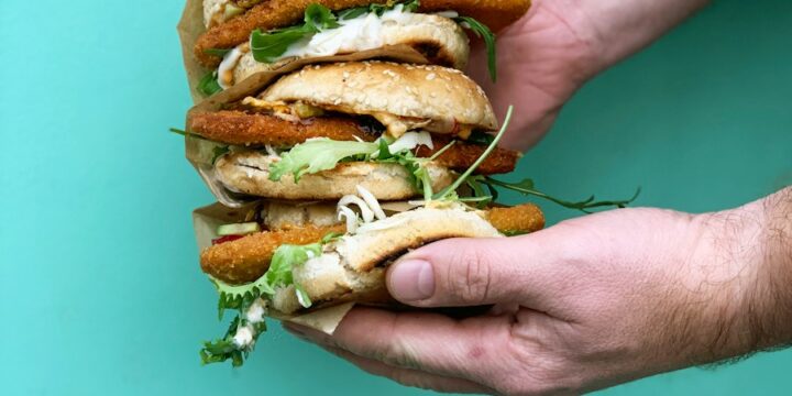 person holding burger with lettuce and tomato